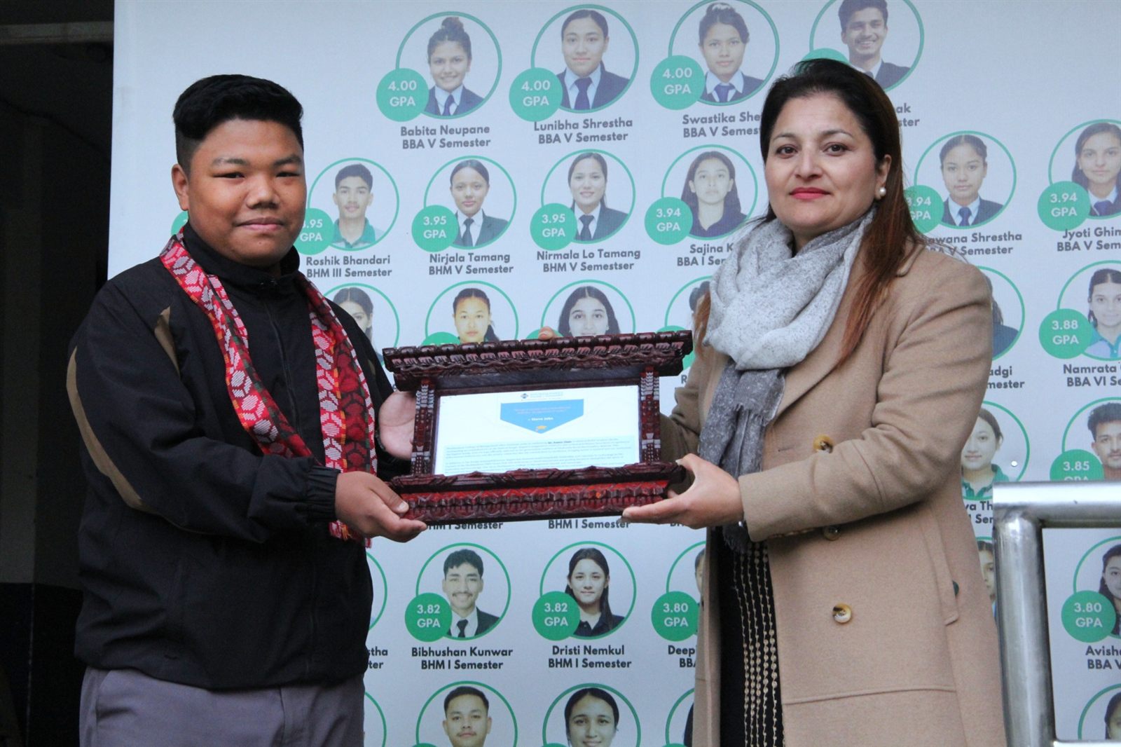 Principal Manita Oli presenting Sugam Ghale with a framed certificate from Shubhashree College of Management in front of a wall of student photos